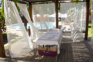 A covered outdoor area with a pool view, a massage table, and a wooden deck.