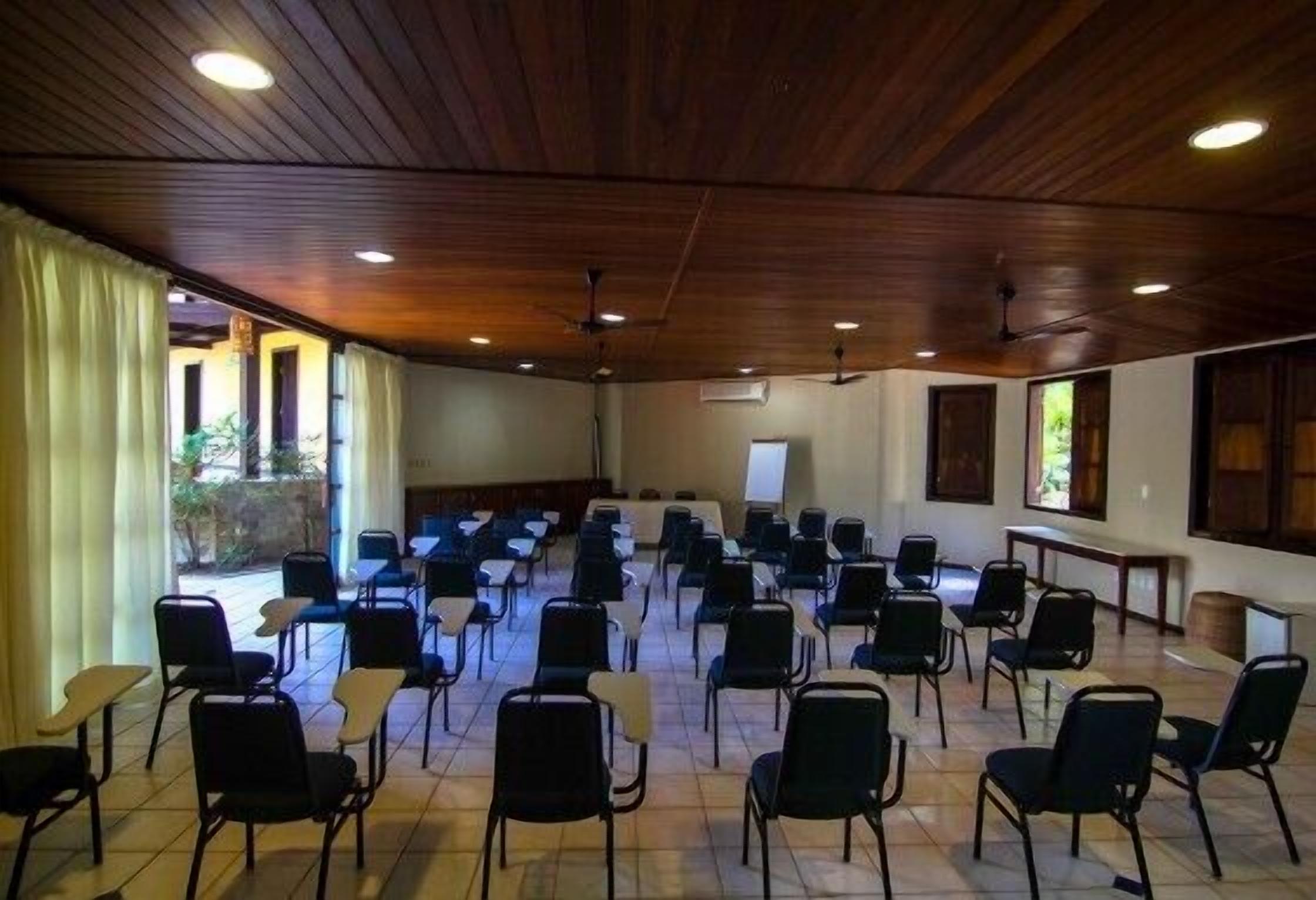 Une salle de conférence avec des rangées de chaises, un plafond en bois et des fenêtres.