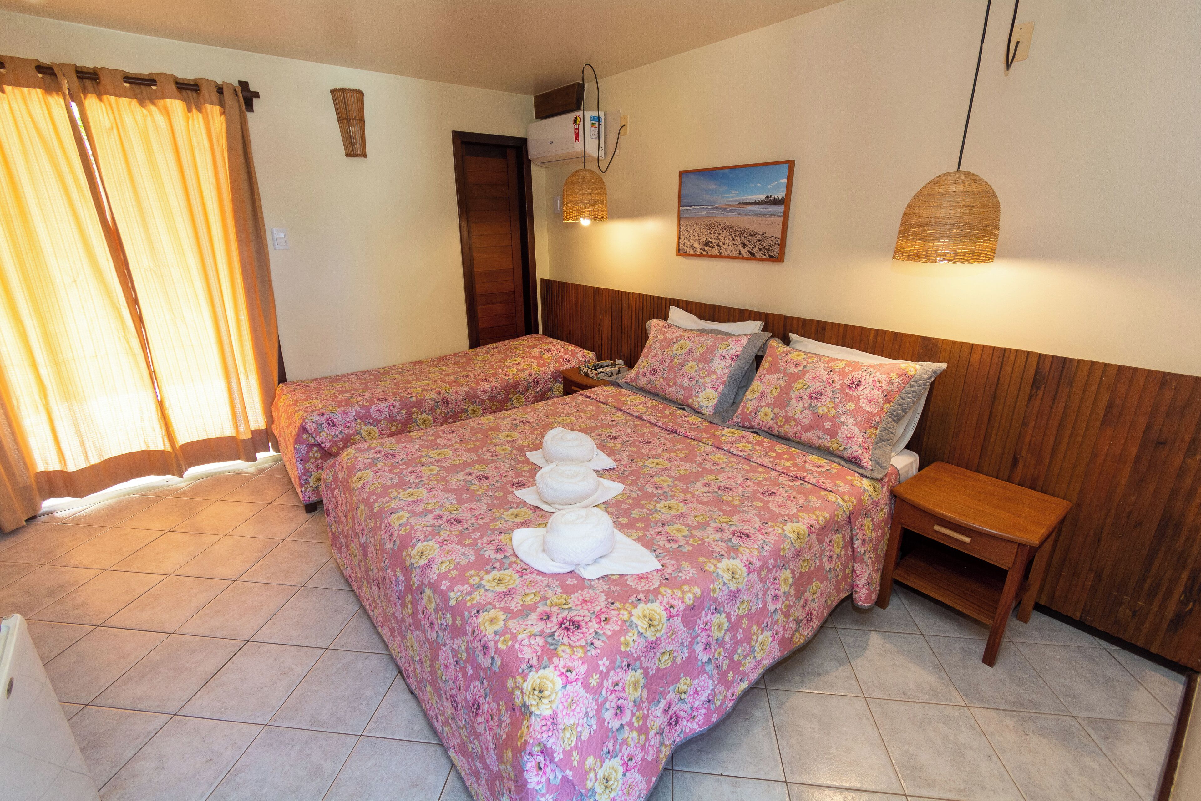 A hotel room with two beds, a wooden headboard, a small bedside table, and a wall-mounted air conditioner.
