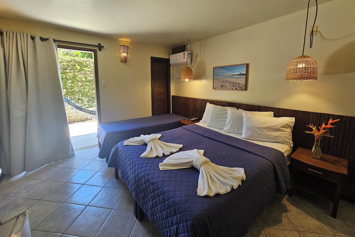A hotel room with a bed, a bedside table, a nightstand, a picture on the wall, and a window with curtains.