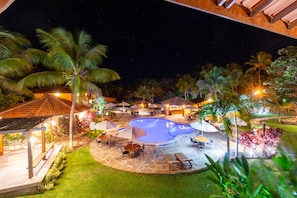 A nighttime pool area with a circular pool, lounge chairs, and umbrellas. - Hotel Pousada Imbassai (Mata de São João)