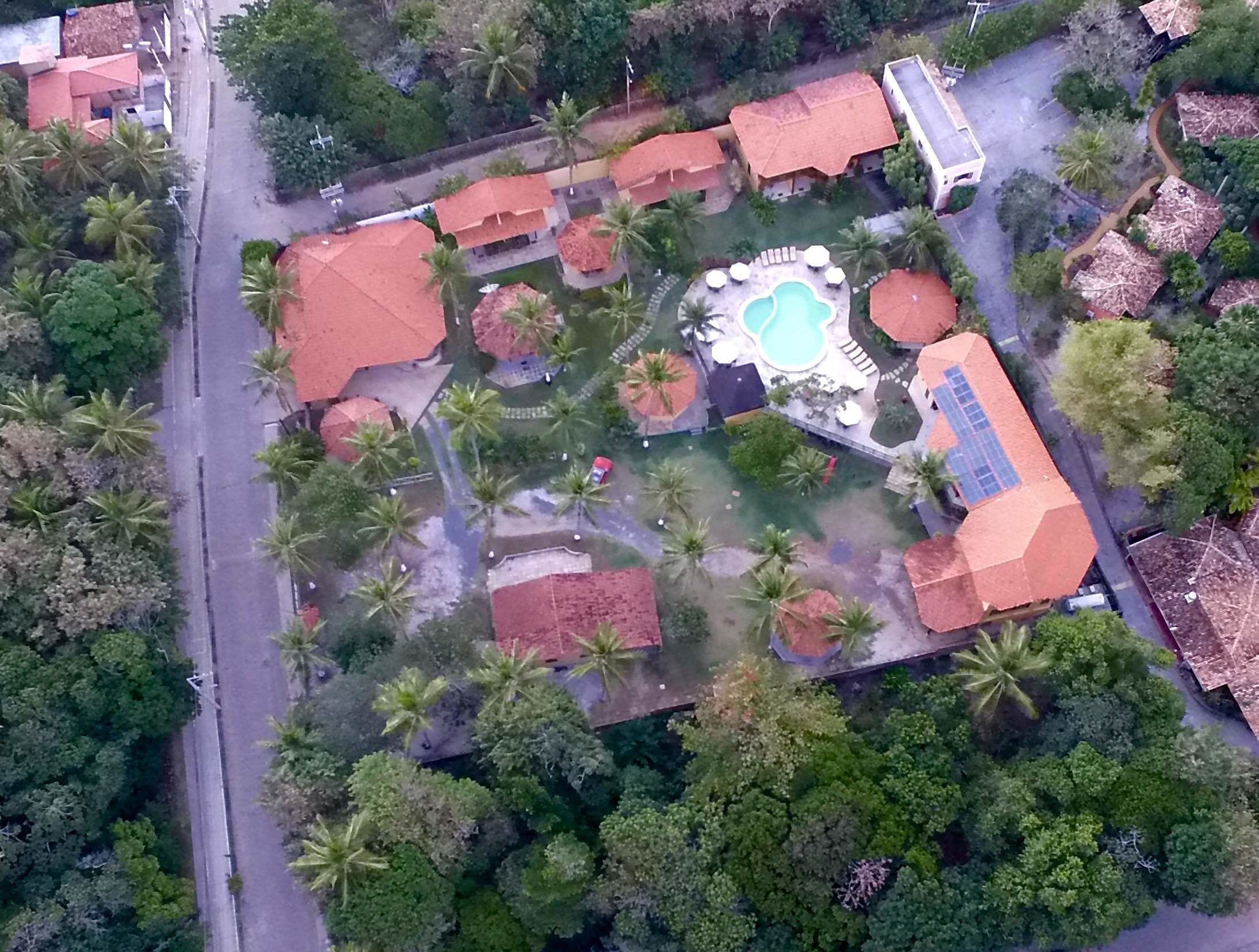 An aerial view of a resort with multiple buildings, palm trees, and a central swimming pool area.