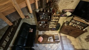 A cozy living room with a black leather sofa, a wooden coffee table, and a variety of decorative items including a shelf with pottery and a television.