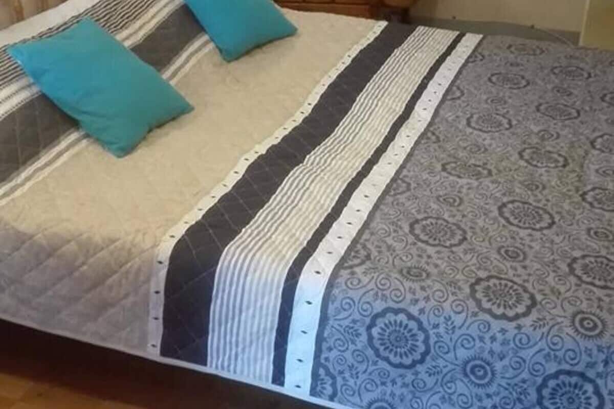 Un lit avec une couvre-lit à rayures et deux oreillers, une chaise en bois et un mur avec un luminaire.
