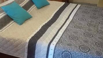 A bed with a striped bedspread and two pillows, a wooden chair, and a wall with a light fixture.