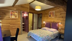 A bedroom with wooden walls, a bed with floral bedding, a desk, and a chair.