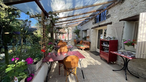 A covered patio with tables and chairs, surrounded by plants and a stone wall.