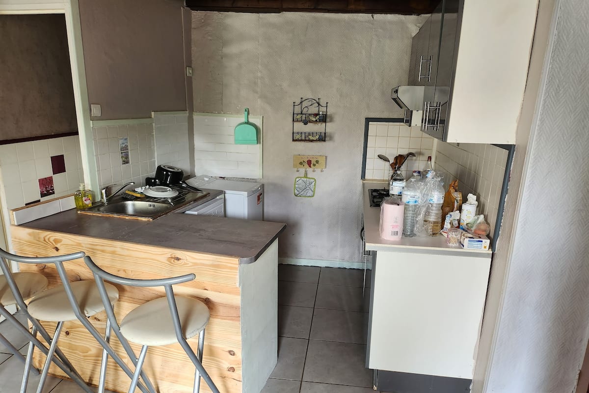 Une cuisine compacte avec un comptoir-bar en bois, deux chaises en métal, un petit réfrigérateur et un évier.