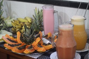 A fruit platter with sliced papaya and pineapple, a pink beverage pitcher, and a glass pitcher with a yellow beverage.