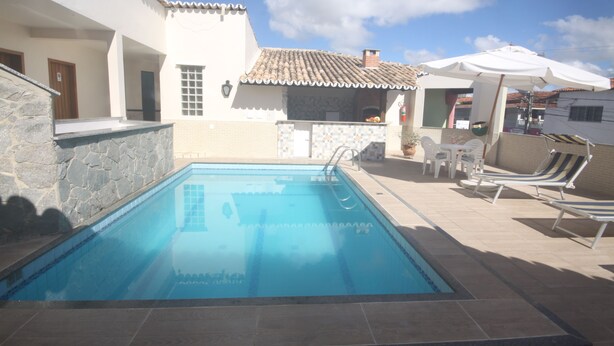 A swimming pool with lounge chairs and umbrellas, surrounded by a building with a tiled roof and stone walls. - Hotel Terra Mater (Porto Seguro)