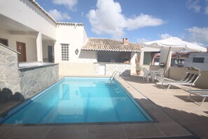 A swimming pool with lounge chairs and umbrellas, surrounded by a building with a tiled roof and stone walls. - Hotel Terra Mater (Porto Seguro)