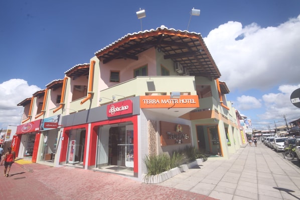 A hotel with a red and beige facade, a sign for 'Terra Mater Hotel', and a storefront with a 'Botecano' sign. - Hotel Terra Mater (Porto Seguro)