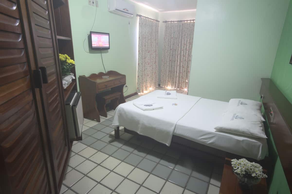 A bedroom with a bed, a desk, a television, and curtains.