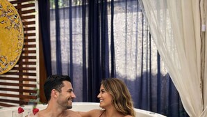Una pareja en un jacuzzi, disfrutando de bebidas, rodeada de paneles de madera y una pared decorativa.