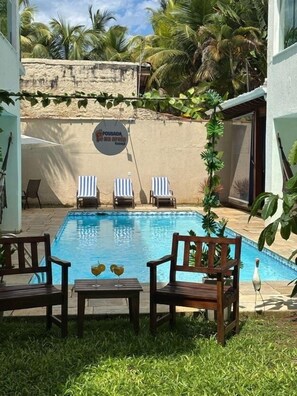 Un espace piscine avec des chaises longues, une table avec des boissons et un panneau indiquant l’emplacement d’un restaurant.