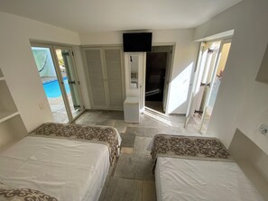 Une chambre avec deux lits, une télévision et une porte coulissante donnant sur un espace piscine.