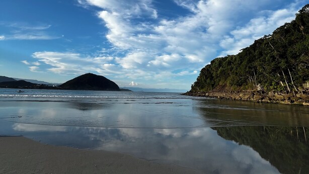 Una playa con cielos despejados, aguas tranquilas y una ladera boscosa.