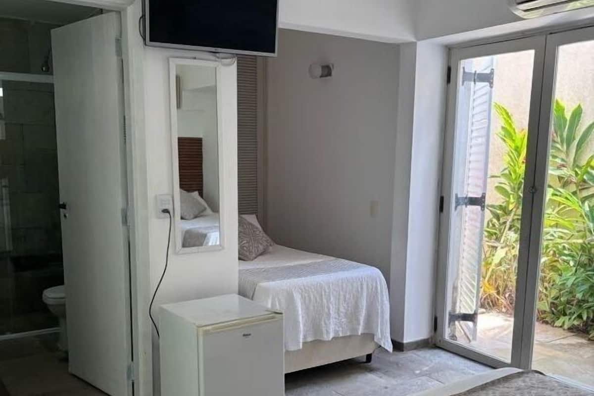 Une chambre à coucher avec un lit, un téléviseur fixé au mur au-dessus du lit, une petite table de chevet et une porte-fenêtre coulissante donnant sur un balcon.