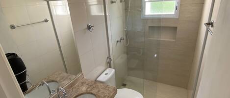 A bathroom with a glass-enclosed shower, a toilet, a sink, and a mirror.