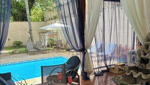 Un espacio al aire libre techado con piscina, muebles de madera y ventilador de techo.