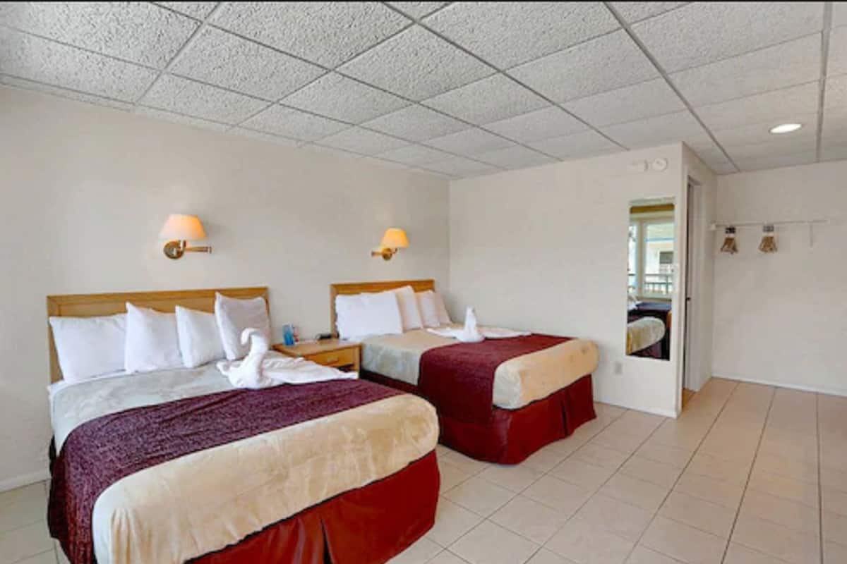 A hotel room with two beds, a wooden headboard, a nightstand, and a bathroom visible through an open door.