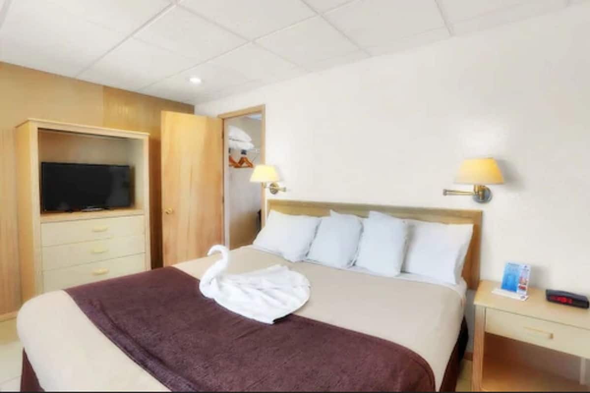 A hotel room with a bed, a TV in a wooden cabinet, a lamp, and a swan-shaped towel on the bed.