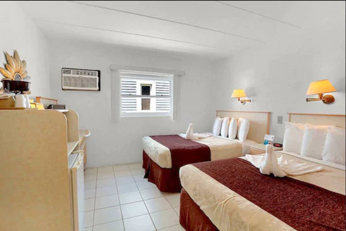 A hotel room with two beds, a small window, and a desk with a lamp.