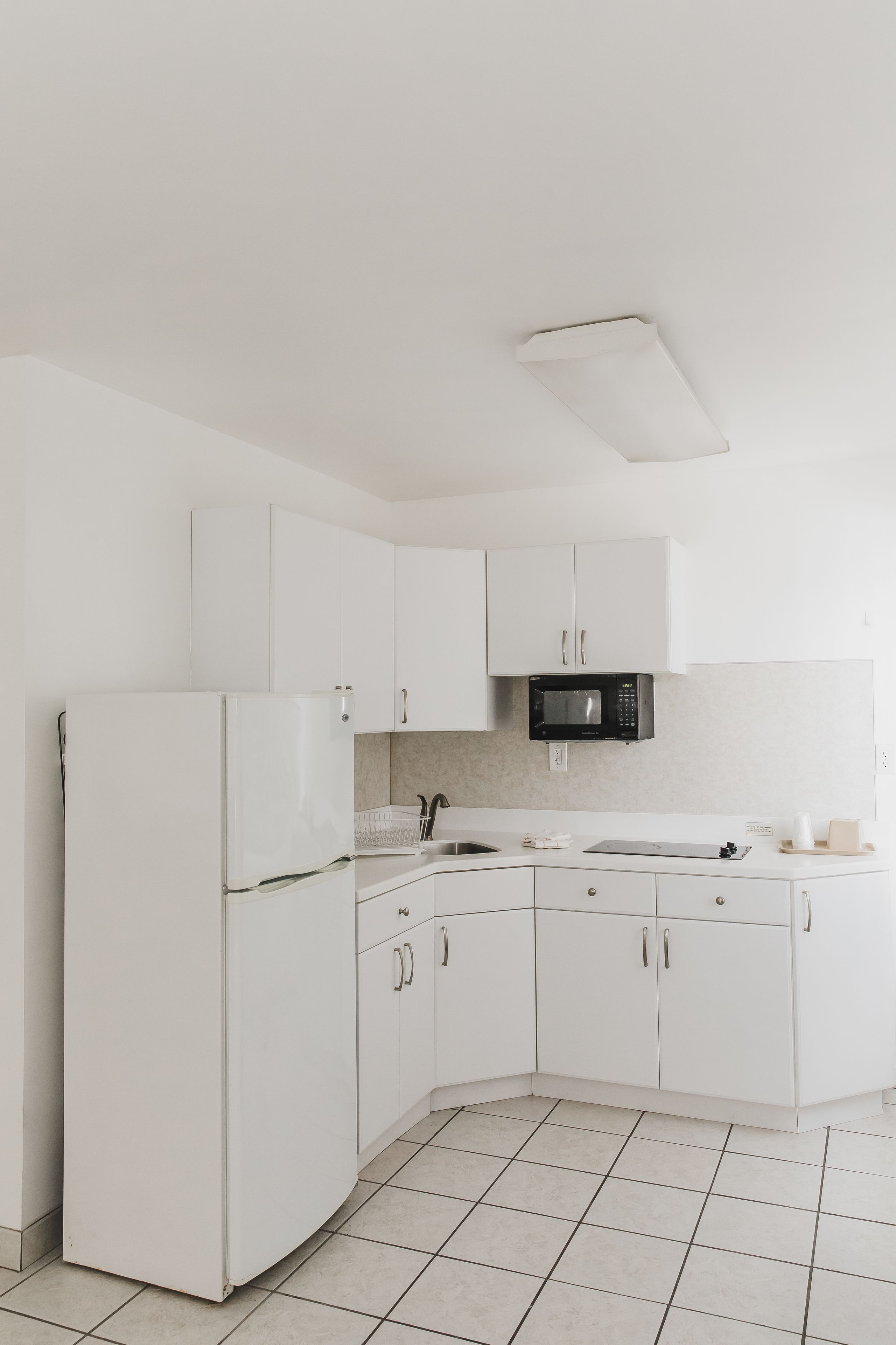 A modern kitchen with white cabinetry, a black microwave, and a stainless steel sink.