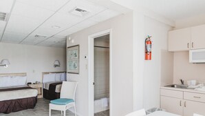 A hotel room with a bed, a chair, a small table, a kitchenette, and a bathroom with a shower. - AA Heart of Wildwood Motels (Wildwood)