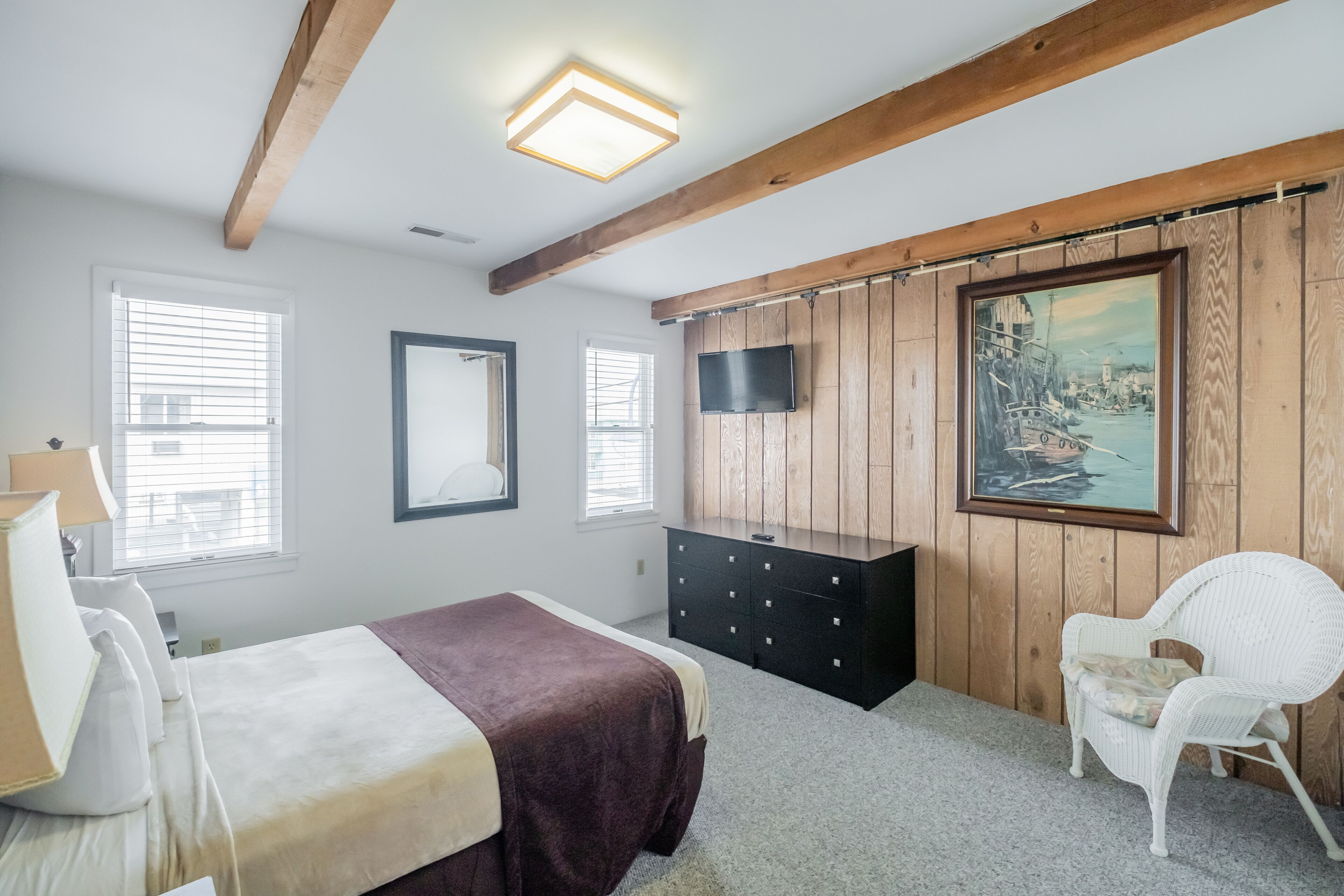 A bedroom with a bed, dresser, chair, and a painting on the wall.