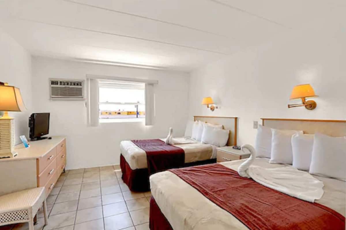 A hotel room with two beds, a desk with a lamp, a television, and a window with a view.