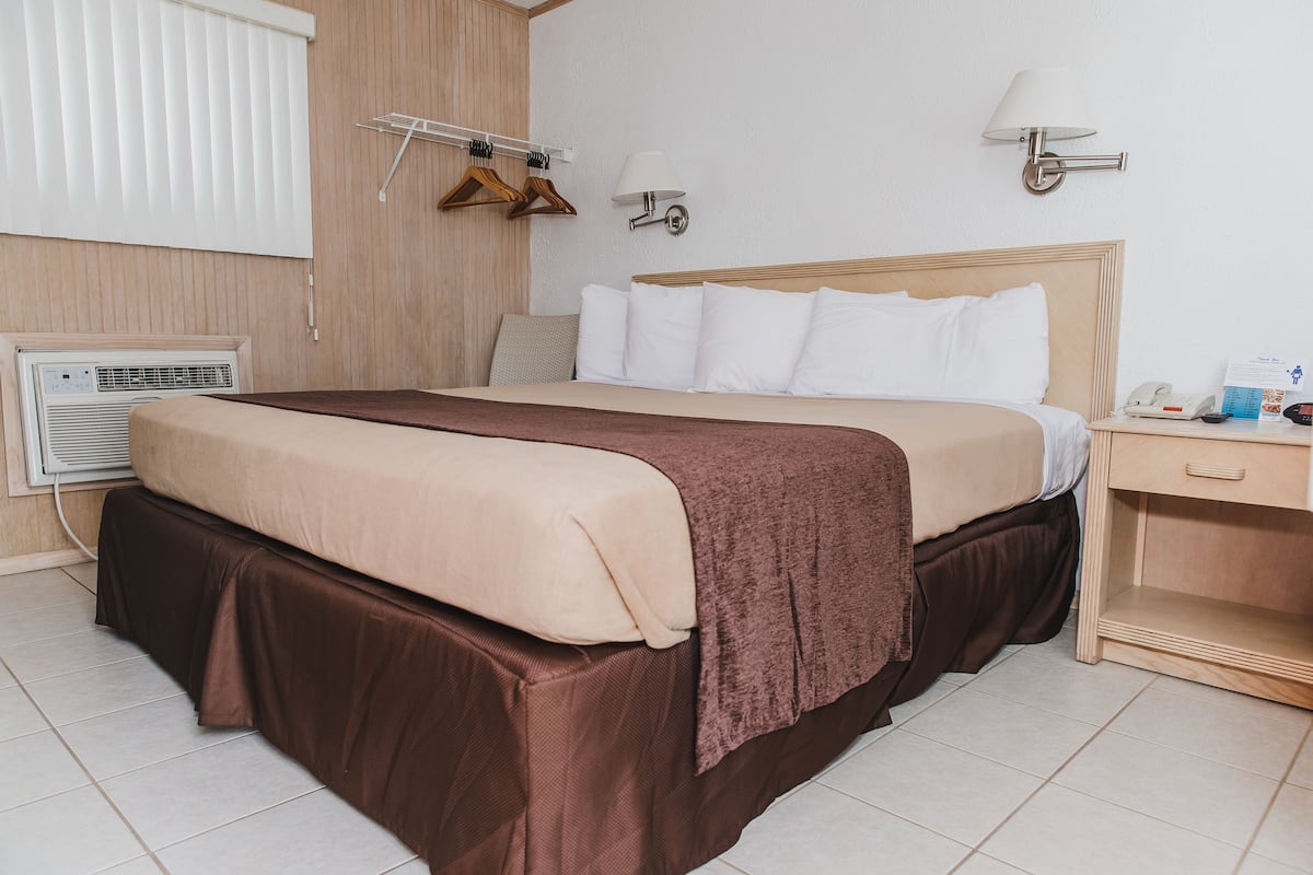 A hotel room with a bed, bedside table, lamp, and a wall-mounted heater.