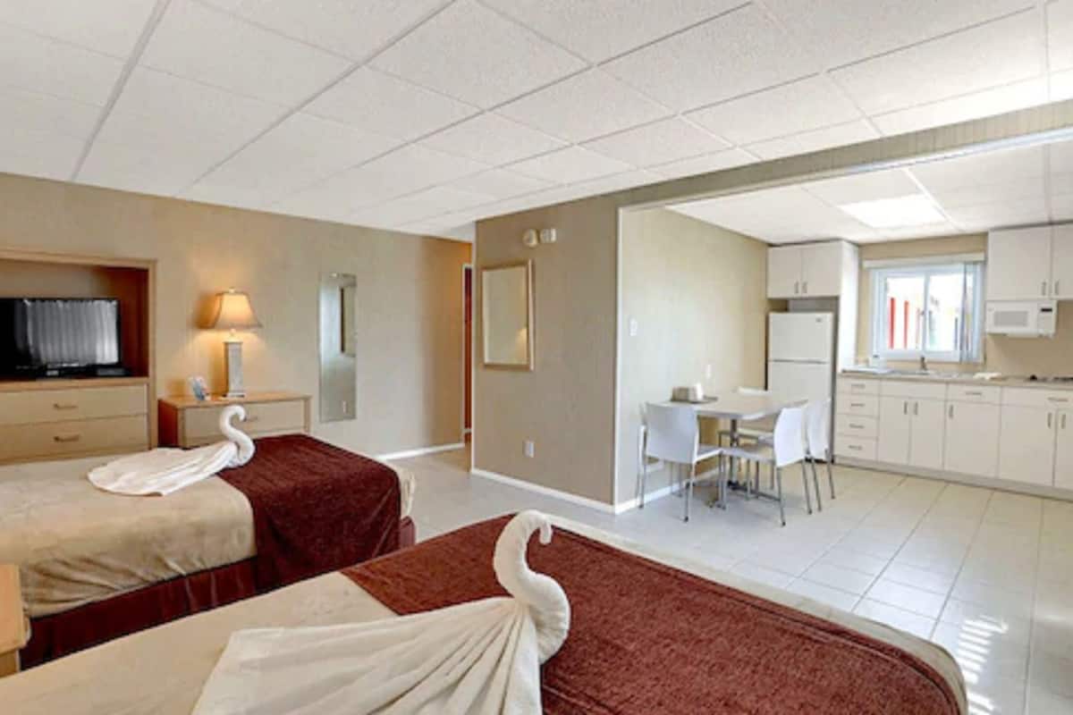 A hotel room with two beds, a desk, and a kitchenette.