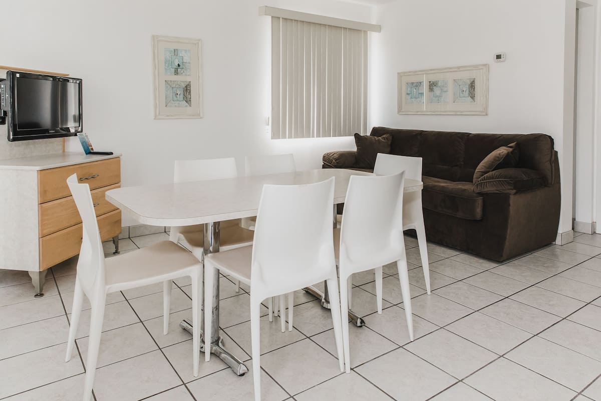 A modern living room with a dining table, white chairs, a brown sofa, and artwork on the walls.