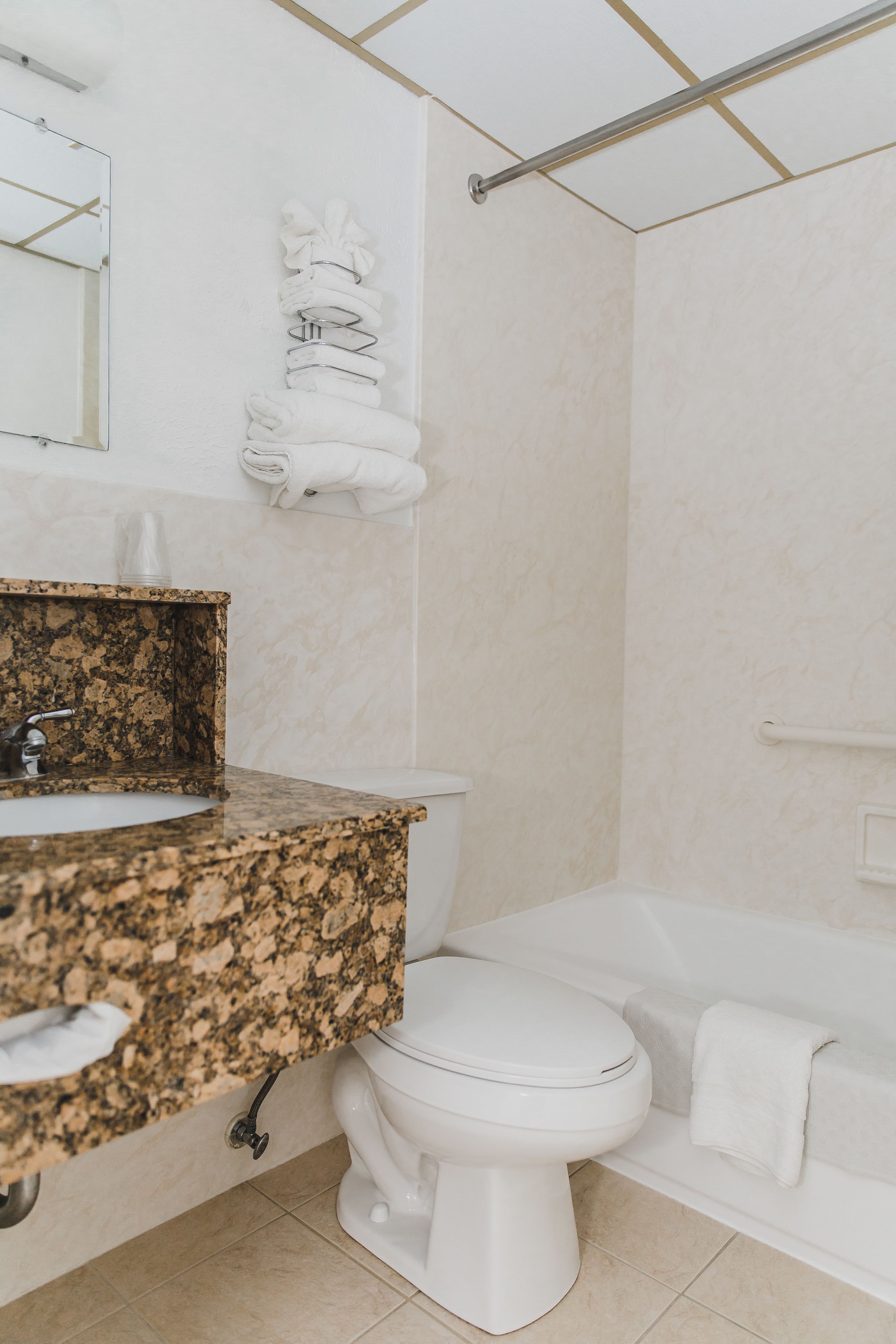 A bathroom with a granite countertop, white toilet, and a bathtub.