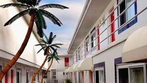 A hotel corridor with palm trees, a staircase, and rooms with red and blue accents. - AA Heart of Wildwood Motels (Wildwood)