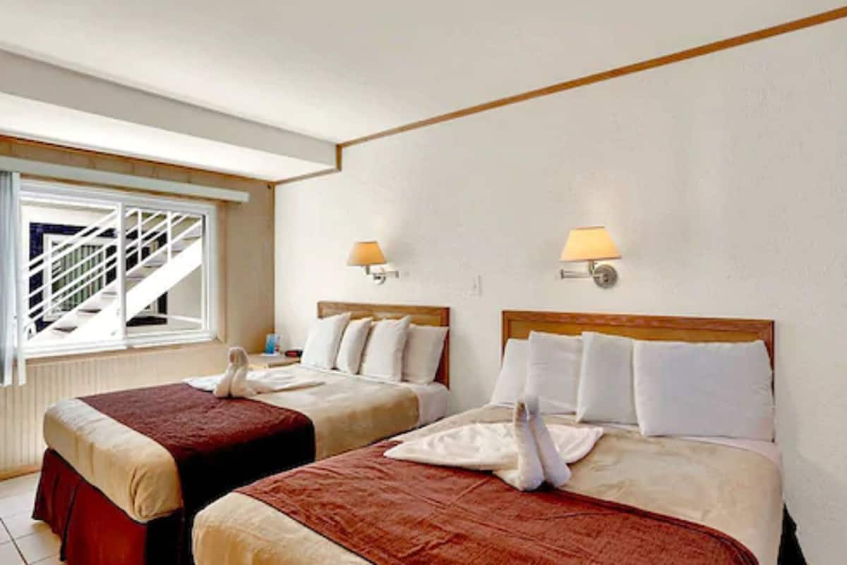 A hotel room with two beds, a staircase, and two wall-mounted lamps.