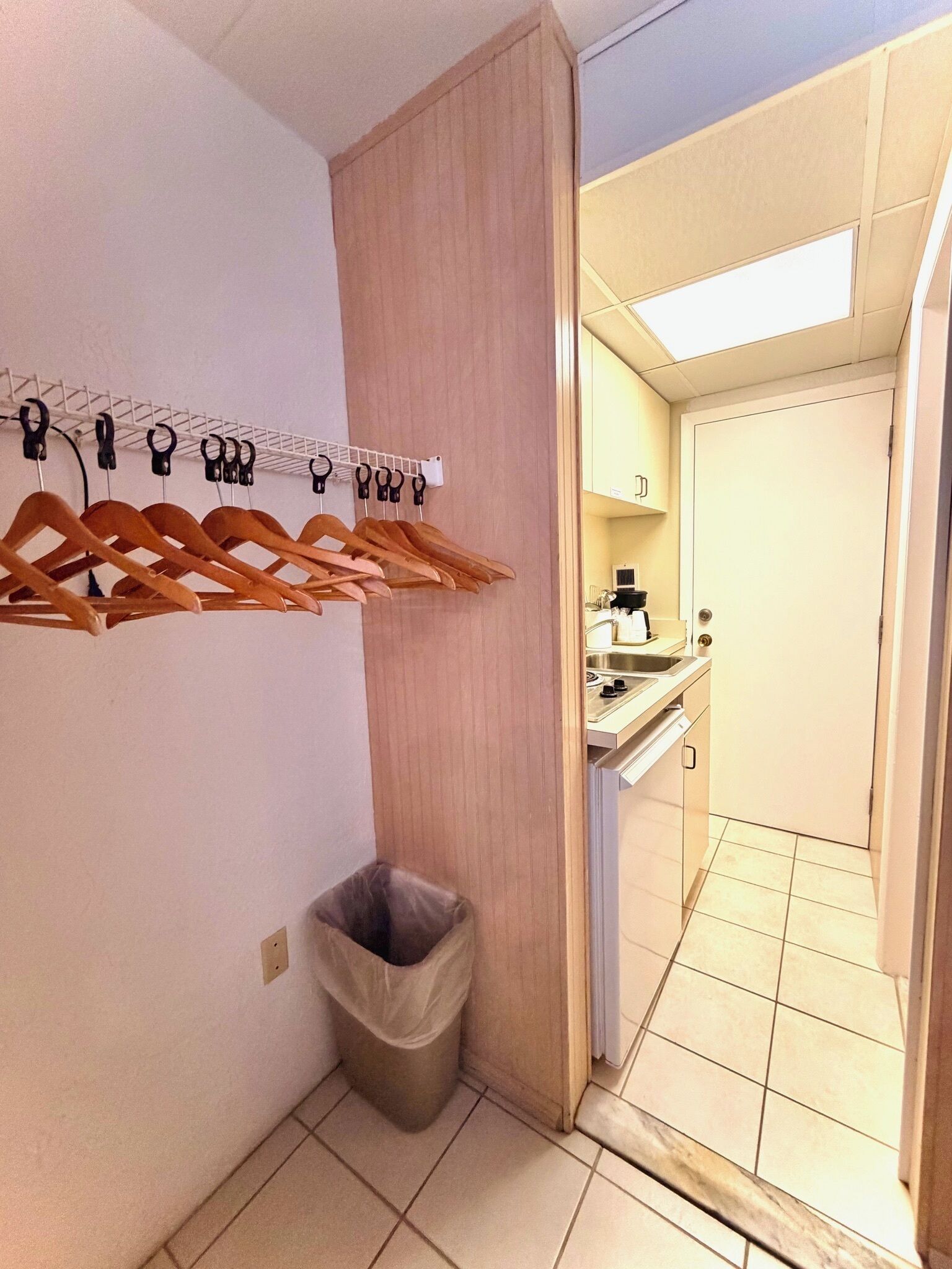 A small bathroom with a wooden cabinet, a towel rack, a trash bin, and a view into a kitchen area.