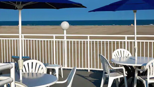 A deck with tables and chairs, overlooking a beach. - AA Heart of Wildwood Motels (Wildwood)