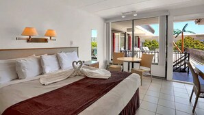 A hotel room with a bed, two bedside lamps, a balcony with a table and chairs, and a view of the outdoors. - AA Heart of Wildwood Motels (Wildwood)