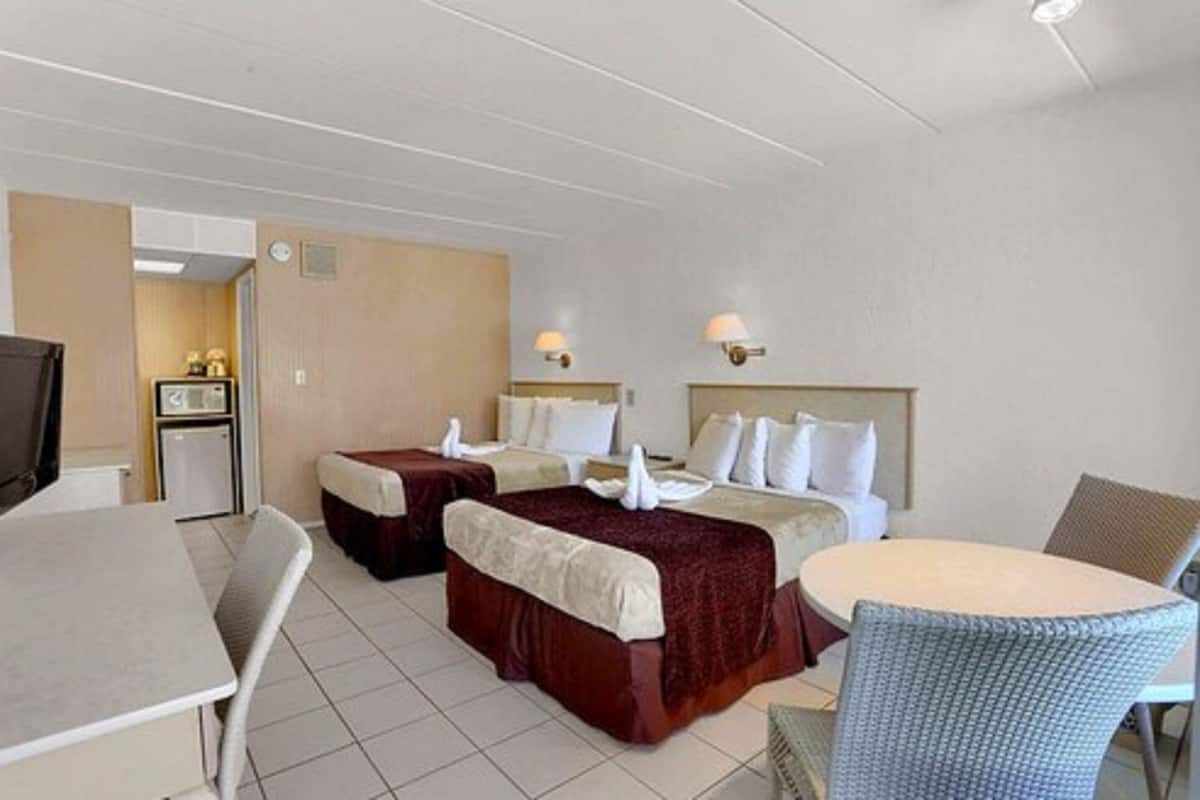 A hotel room with two beds, a small kitchenette, a dining table, and a TV.
