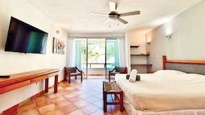Habitación de hotel con cama, escritorio, silla, televisor y balcón con vista a palmeras.