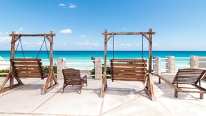 Un columpio de madera con bancos, con vistas a una playa de aguas azules y transparentes.