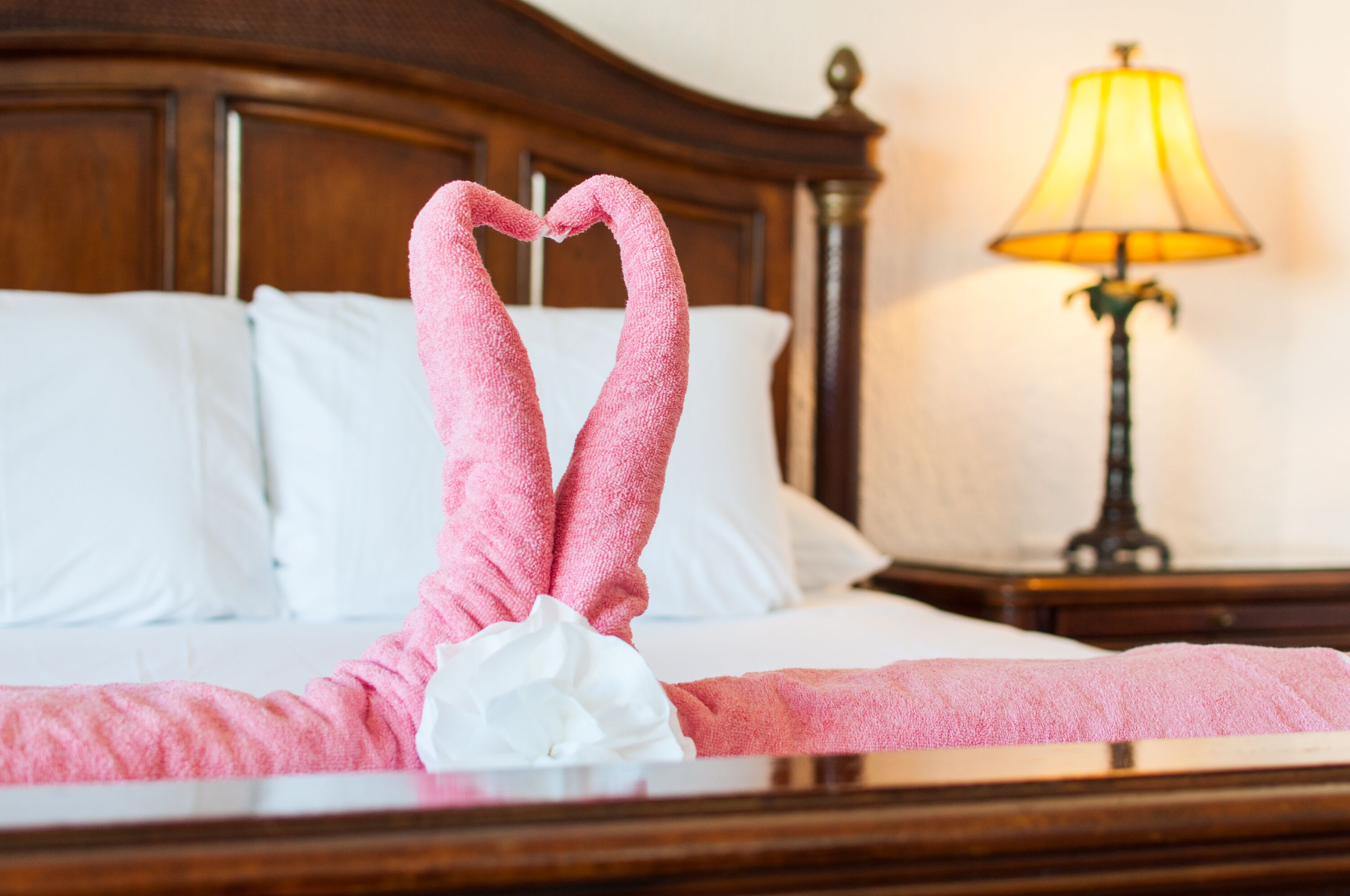 A neatly made bed with pink towels arranged in a heart shape and a white flower.