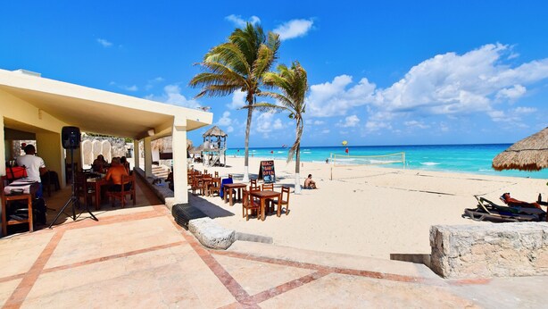 Un restaurante frente a la playa con terraza al aire libre, palmeras y vista al océano.