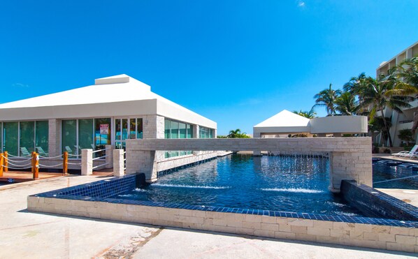 A modern hotel with a pool area, featuring a clear blue sky and palm trees.