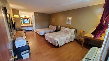 A hotel room with two beds, a desk, a chair, a mirror, a window, and a small kitchenette.