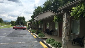 A motel with a parking lot, a red car parked in the lot, and a stone pillar with a planter. - Chatuge Mountain Inn (Hayesville)