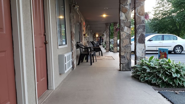 A covered walkway with stone pillars, a row of chairs, and a parked car. - Chatuge Mountain Inn (Hayesville)