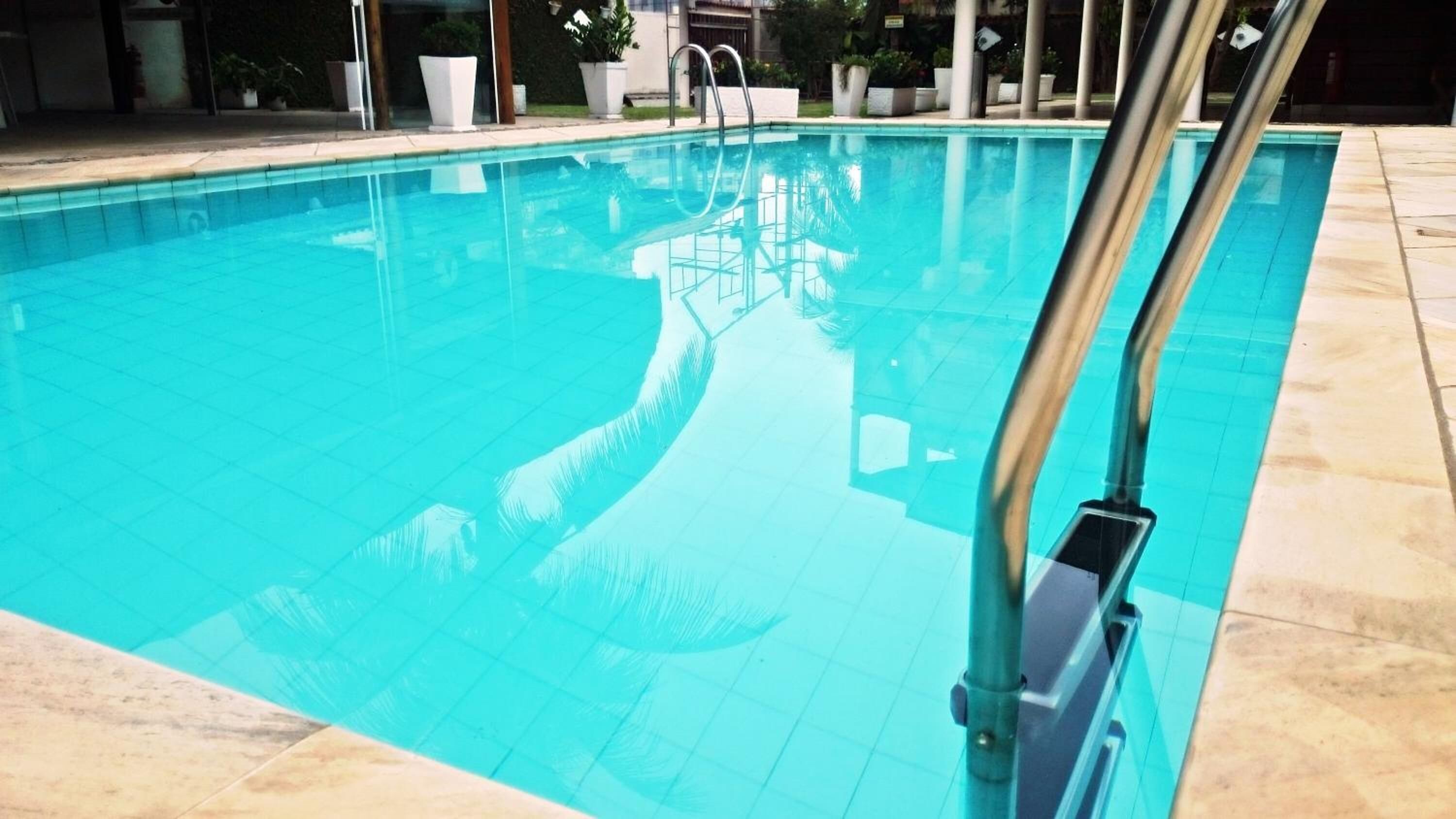 Une piscine à l’eau d’un bleu cristallin, avec une échelle en métal et une terrasse carrelée.